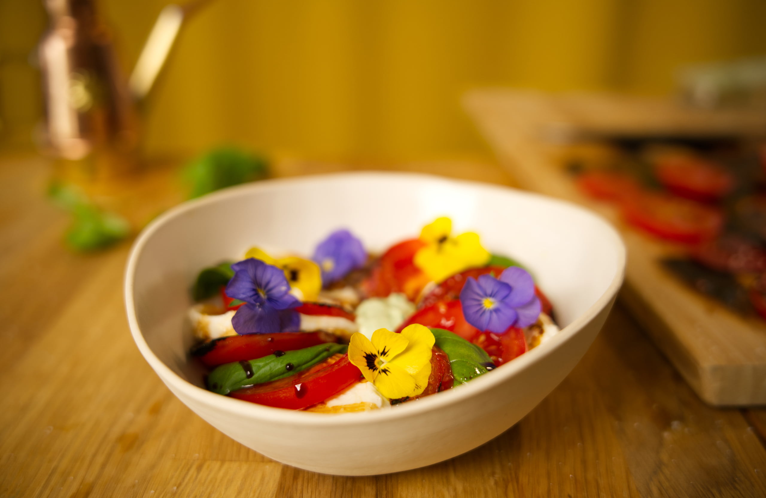 Kuvassa on valkoisella syvällä lautasella insalata capreseä, joka on koristeltu syötävillä orvokeilla.