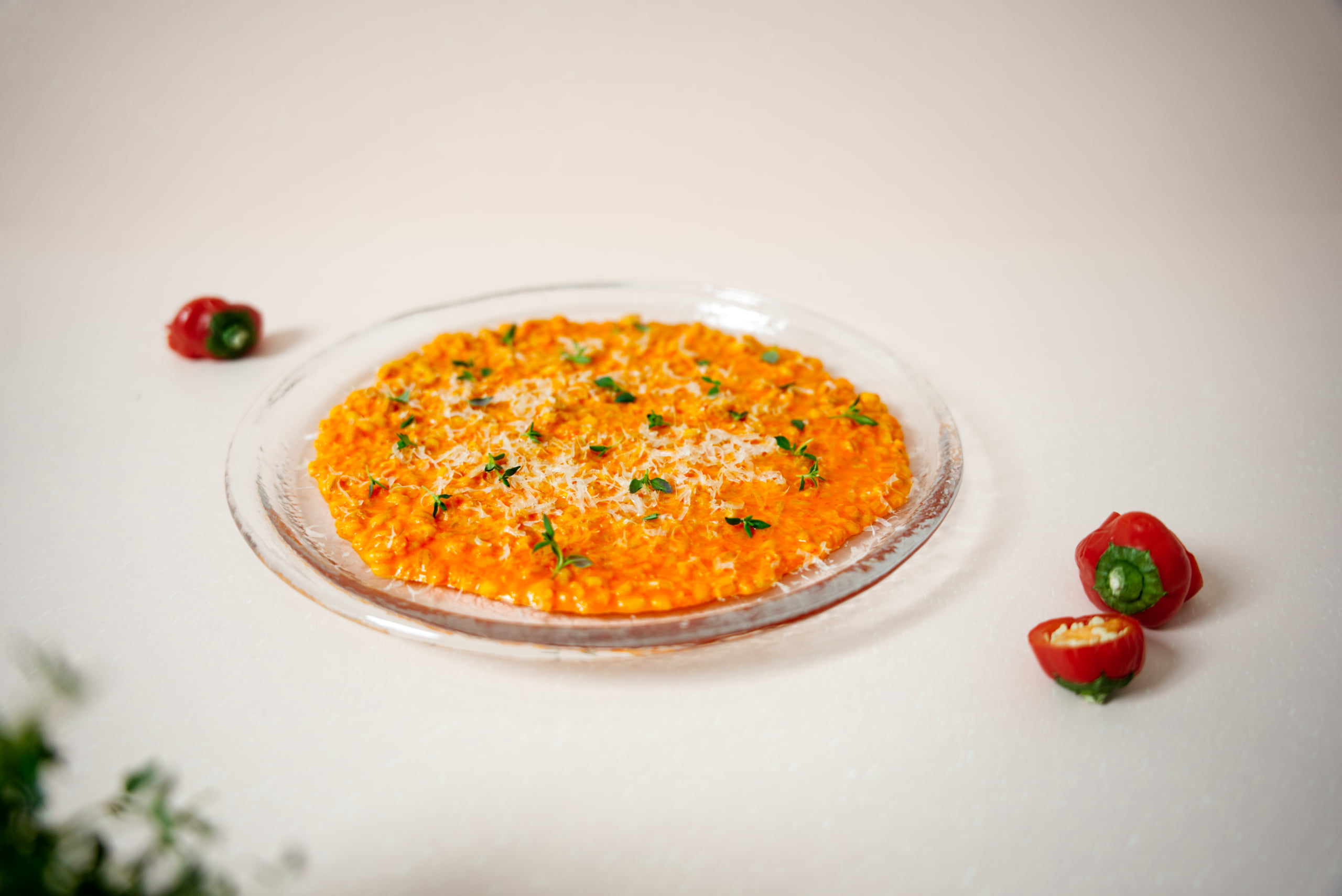 Kuvassa on lasisella lautasella paprika-ohrarisottoa. Kuvan tausta on valkoinen