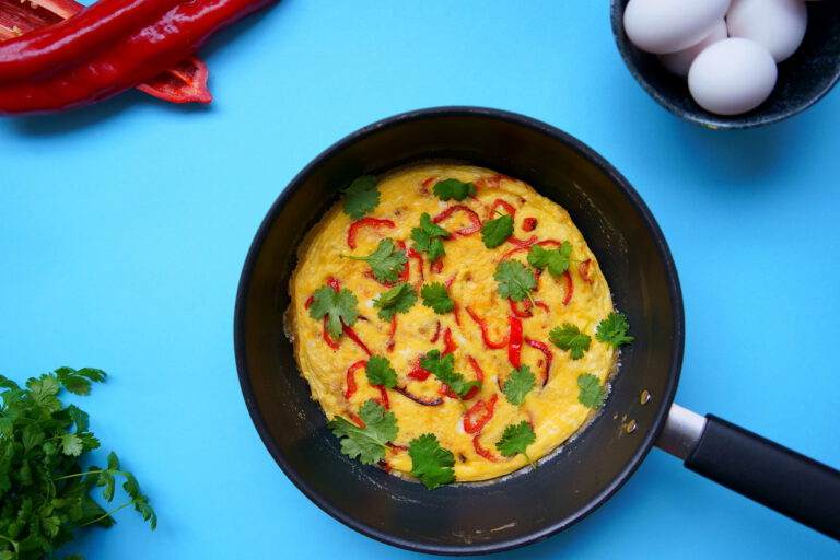Kuvassa on paistinpannulla paprikafrittata. Kuvan tausta on sininen.